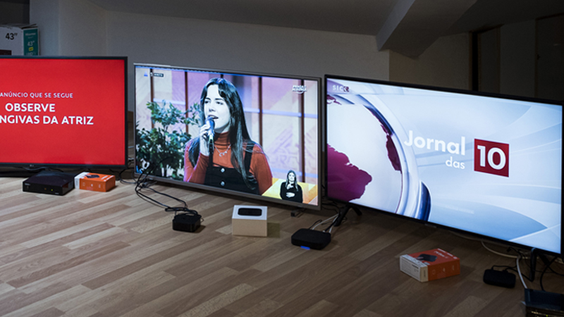 Três monitores instalados lado a lado, exibindo imagens dos serviços de televisão